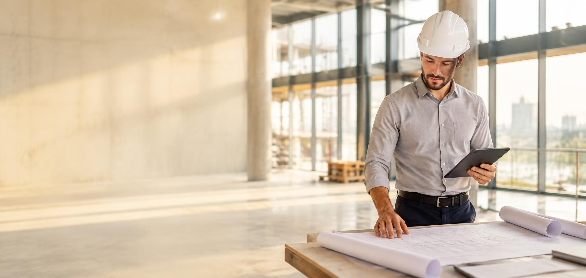 Construction estimator reviewing blueprints and a tablet inside a commercial building under construction